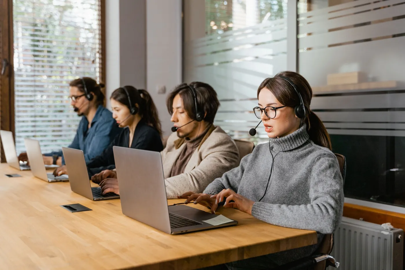 Call centre agents wearing headsets working on laptops at a shared desk