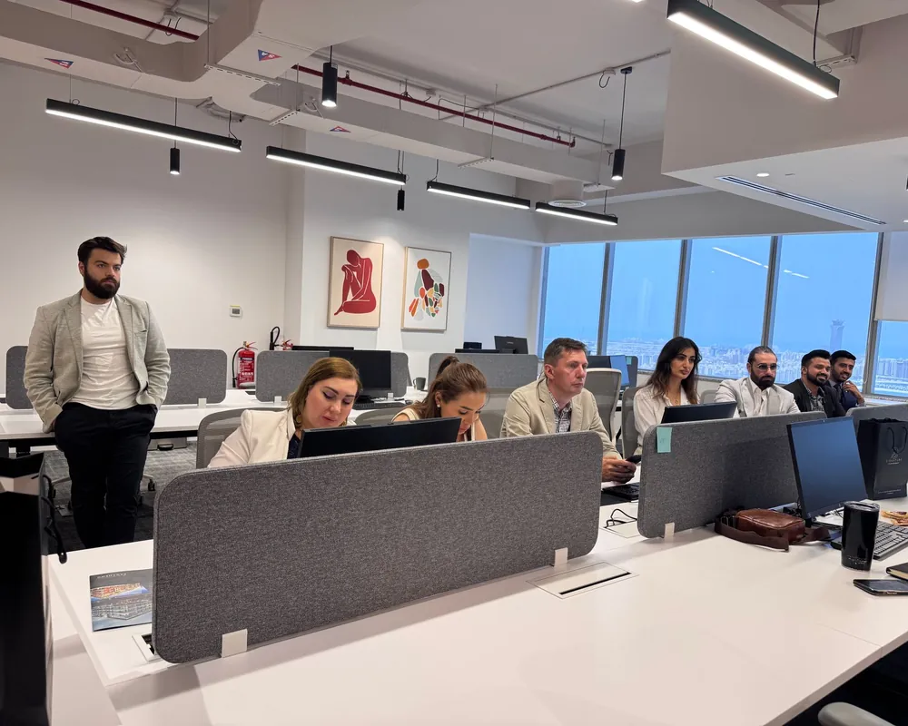 Bright open-plan office floor with rows of desks and monitors and a team leader standing by